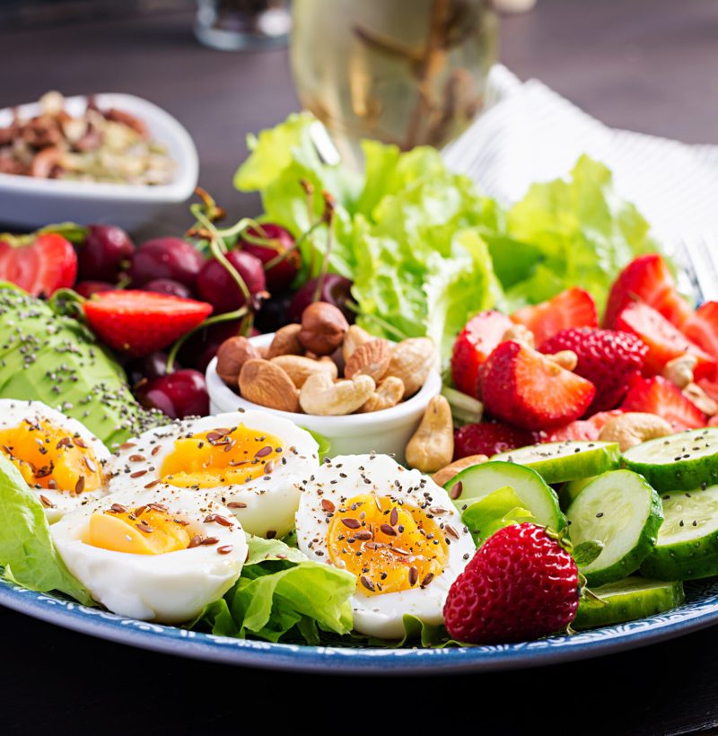 Plate with a paleo diet food. Boiled eggs, avocado, cucumber, nuts, cherry and strawberries. Paleo breakfast.